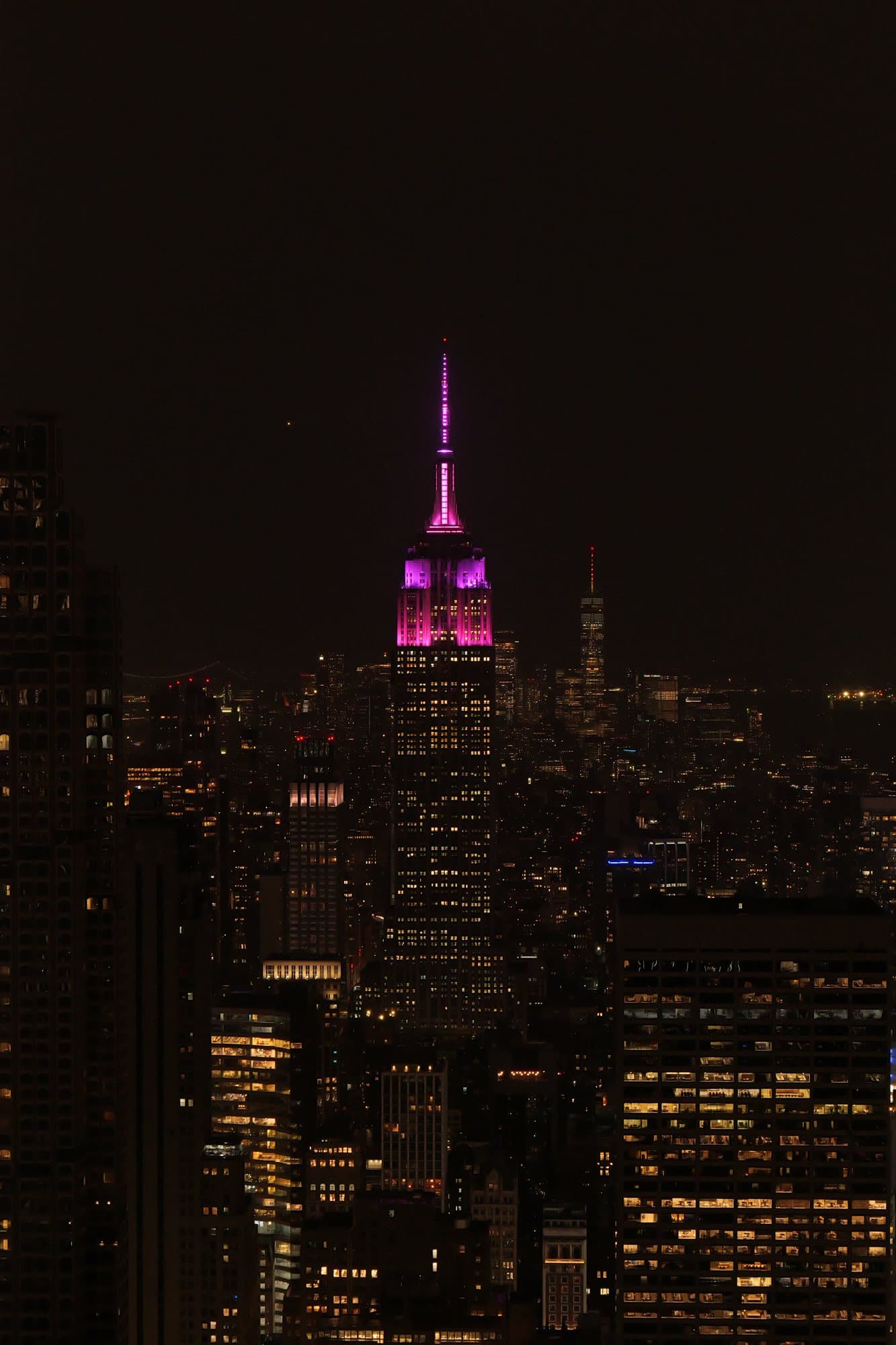 Night city skyline with illuminated buildings and a magenta-lit landmark